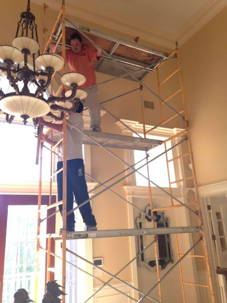 Technicians on scaffolding treating the ceiling line in a two-story entry